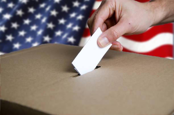 istock Hand putting USA voting card in ballot box 1440297319
