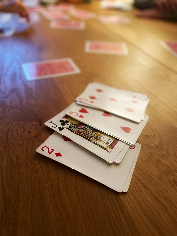 Playing cards laid on a wooden table in the foreground with some of the deck of cards in the background