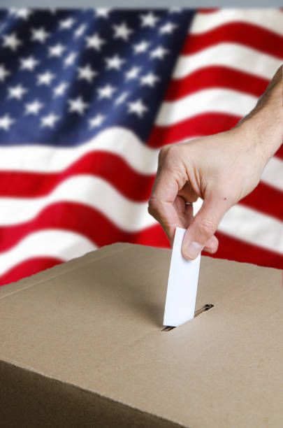 istock Hand putting USA voting card in ballot box 1440297474
