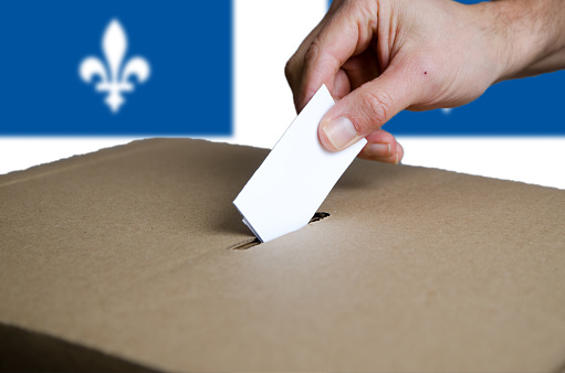 Hand putting Quebec voting card in ballot box\nQuebec flag in background