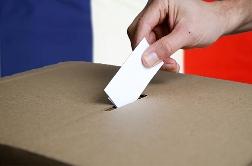 Hand putting France voting card in ballot box\nFrance flag in background