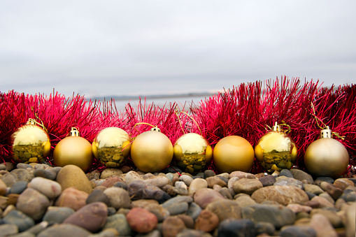 Christmas toys - golden balls on the beach, blurred sea in the background. New Year or Christmas card, invitation with copy space for text.