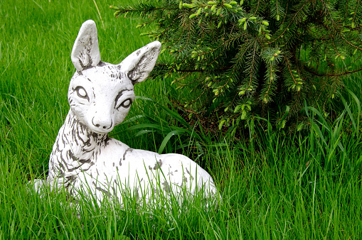 Stone white deer bambi sculpture lying on the green lawn.