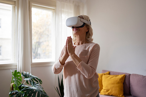 Senior woman meditating in the morning with virtual reality headset at cosy home living room