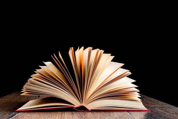 istock An open book with a hardcover on a wooden surface against a dark background. 1440308964