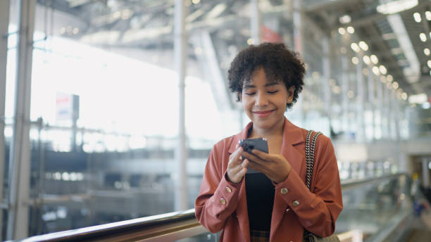 donna asiatica che legge messaggi di testo e sorride all'aeroporto - airport airplane travel airport lounge foto e immagini stock