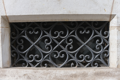 Close-up of a cellar window barred with ornate forged metal iron wrought iron as decoration in a historic facade of bright stone concept for blacksmith art and ancient craftsmanship
