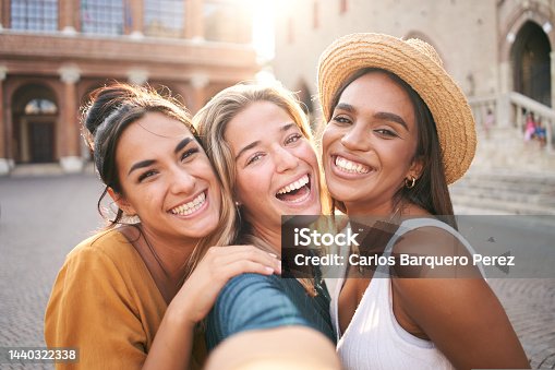istock Three young smiling hipster women in summer clothes. Girls taking selfie self portrait photos on smartphone.Models posing in the street.Female showing positive face emotions 1440322338