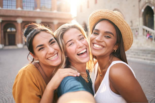Three young smiling hipster women in summer clothes. Girls taking selfie self portrait photos on smartphone.Models posing in the street.Female showing positive face emotions stock photo