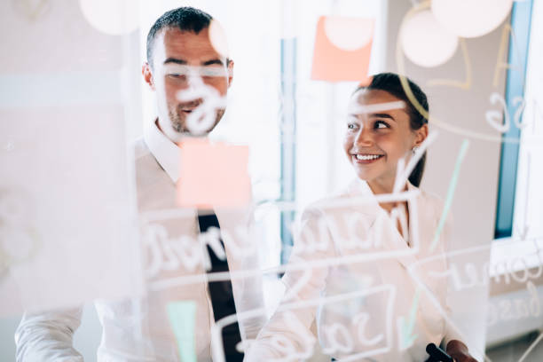 istock Successful male and female partners talking while making business presentation on glass board at office briefing, young economists analyzing information togetherness at brainstorming corporate meeting 1440324291