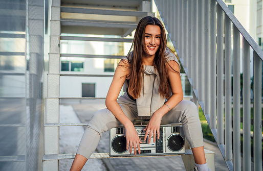 Young smiling woman sitting on the stairs with a boombox in the city