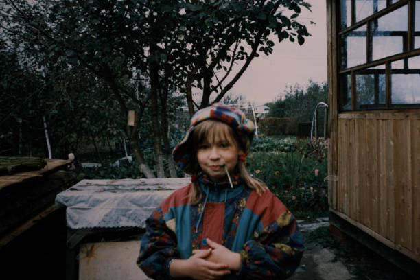 a garotinha usando roupas quentes está parada no quintal e olhando para a câmera. foto vintage - 1991 - fotografias e filmes do acervo
