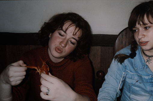Two sisters are sitting at the café and one of them playing with cooked lobster. Vintage photo