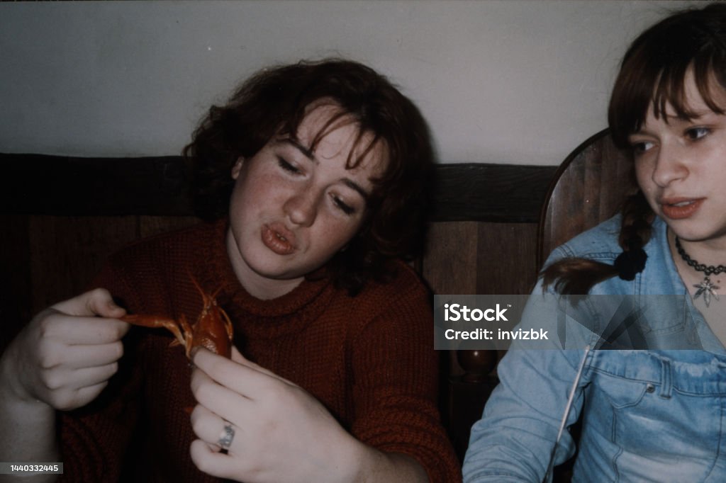 Two sisters are sitting at the cafe and one of them playing with cooked lobster. Vintage photo Two sisters are sitting at the café and one of them playing with cooked lobster. Vintage photo 1990-1999 Stock Photo