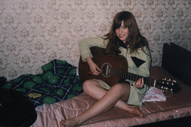 teenage girl is sitting on bed and playing guitar. vintage home photo - tiener fotos stockfoto's en -beelden