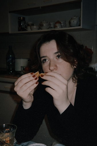 La joven está sentada a la mesa y comiendo una mandarina. Foto vintage photo