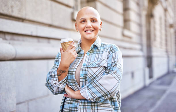 Bald woman, coffee and motivation of strong, proud and independent cancer free female standing outdoor on city street with a smile. Happy girl with positive mindset, tea and joy on urban street stock photo