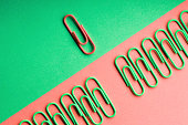 Green paper clips in a row. One different unique red paperclip.