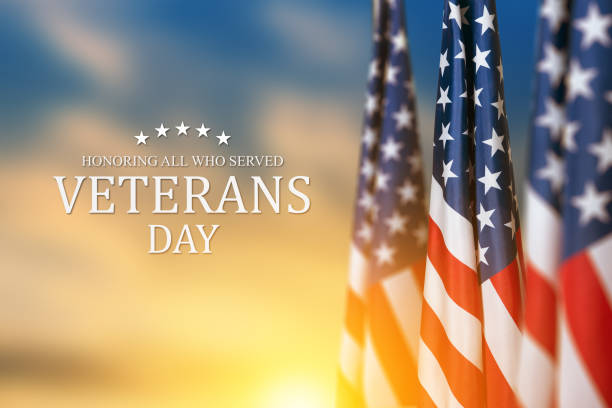 American flags with Text Veterans Day Honoring All Who Served on sunset background.