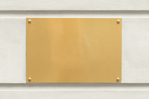 A blank golden sign outdoors on the wall of an office building.