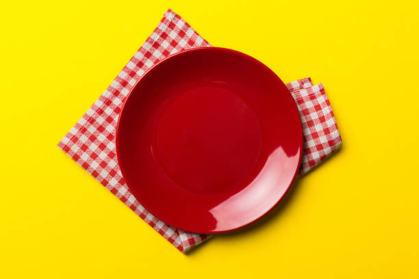 Top view on colored background empty round red plate on tablecloth for food. Empty dish on napkin with space for your design
