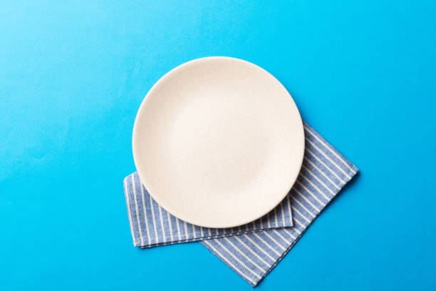 istock Top view on colored background empty round white plate on tablecloth for food. Empty dish on napkin with space for your design 1440346134