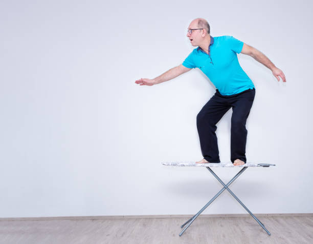 A Caucasian man stands on an ironing board and introduces himself as a surfer. Pre-vacation workout. A Caucasian man stands on an ironing board and introduces himself as a surfer. Pre-vacation workout. negative space illusion stock pictures, royalty-free photos & images