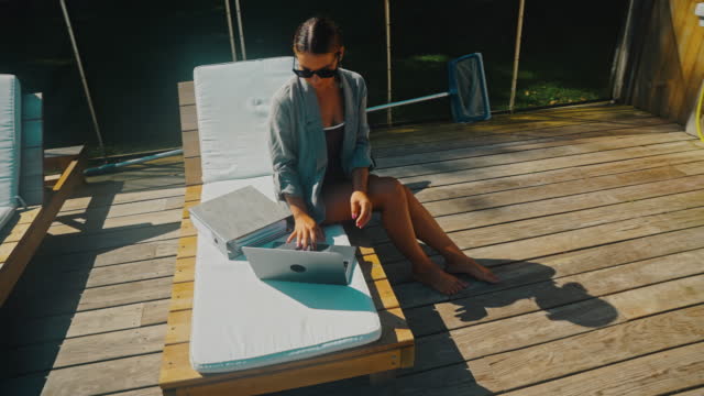 WS Young woman uses a laptop while she works by the swimming pool