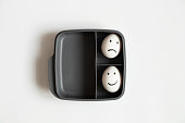 istock Two eggs with a joyful smile and a sad one lie in a plastic container on a white background, a choice of joy and sadness 1440350411