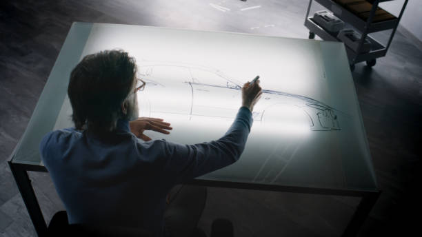 Senior designer drawing new car sketch with marker Senior automotive male designer drawing sketch blueprint with marker at the light table, developing futuristic electric car future design. He working in modern car design development studio. industrial designer stock pictures, royalty-free photos & images