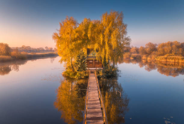 old fisherman house and wooden pier at sunrise in autumn. aerial view. beautiful landscape with house on small island on the lake, colorful trees, jetty, reflection in water. fall in ukraine. top view - coastline aerial view forest pond imagens e fotografias de stock