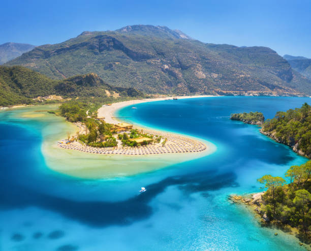 Aerial view of sea bay, sandy beach with umbrellas, trees, mountain at sunny day in summer. Blue lagoon in Oludeniz, Turkey. Tropical landscape with island, white sandy bank, blue water. Top view stock photo