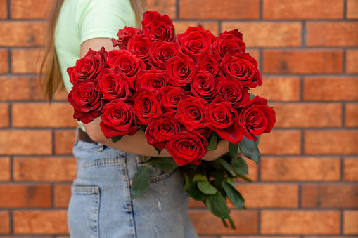 Woman holding luxury bouquet of fresh red roses against the background of brick wall. Mono bouquet of red roses in womans hands.