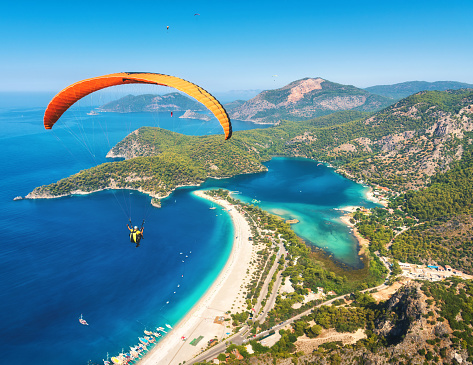 Paragliding in the sky. Paraglider tandem flying over the sea with blue water and mountains in bright sunny day. Aerial view of paraglider and Blue Lagoon in Oludeniz, Turkey. Extreme sport. Landscape