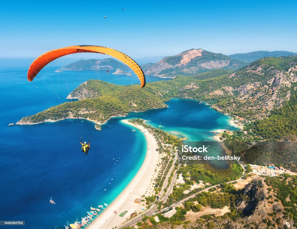 Paragliding in the sky. Paraglider tandem flying over the sea with blue water and mountains in bright sunny day. Aerial view of paraglider and Blue Lagoon in Oludeniz, Turkey. Extreme sport. Landscape Aerial View Stock Photo