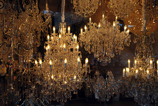 A showcase full of lighted chrystal chandeliers shimmering in shades of gold, hanging at an art and furniture shop. Classic designer chandelier.