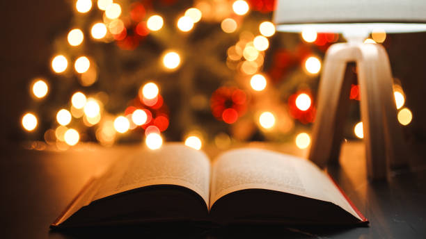 istock Open book on a table in front of Christmas tree during night 1440358797