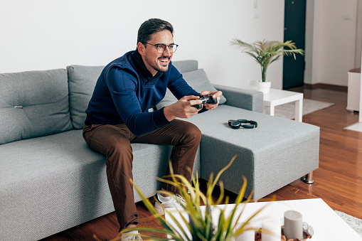 An attractive mid adult Caucasian man sitting alone on sofa and playing video games