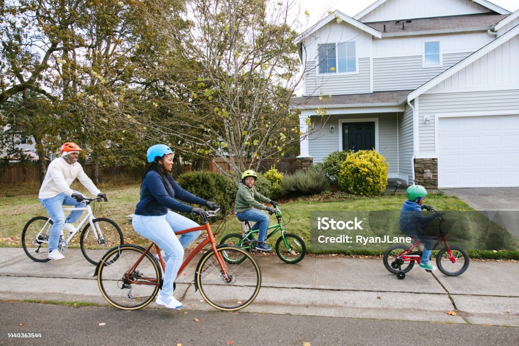 Family Riding Bicycles On Neighborhood Street A young African American family enjoys a fun time of family exercise, riding bikes together on a cool Autumn day.  Healthy lifestyle and good childhood memories. Community Stock Photo