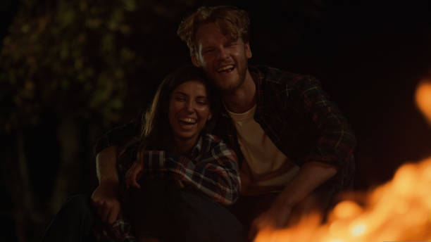 istock Fun couple laugh together on night camp site. Smiling millennials date romantic. 1440363829