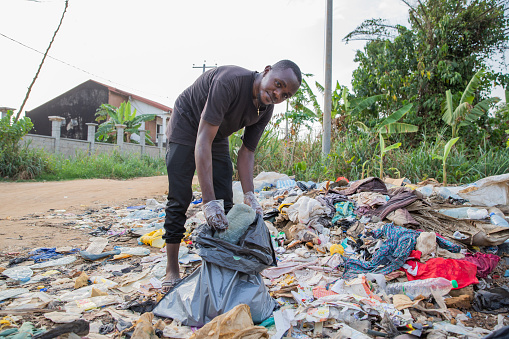 Young african man looks at the camera while collecting waste from the ground.