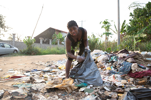 Young African girl picks up garbage thrown there in the open air. Pollution concept.