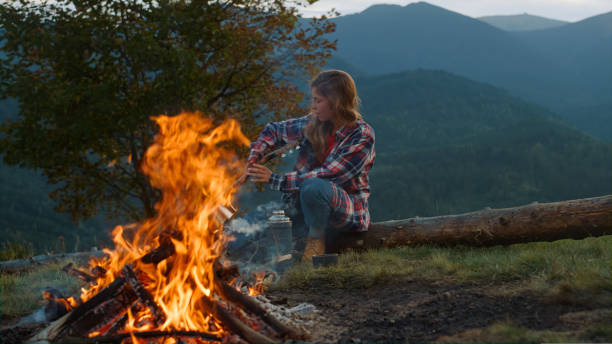 istock Active woman spend evening by bonfire. Young hiker play guitar in mountains. 1440366931