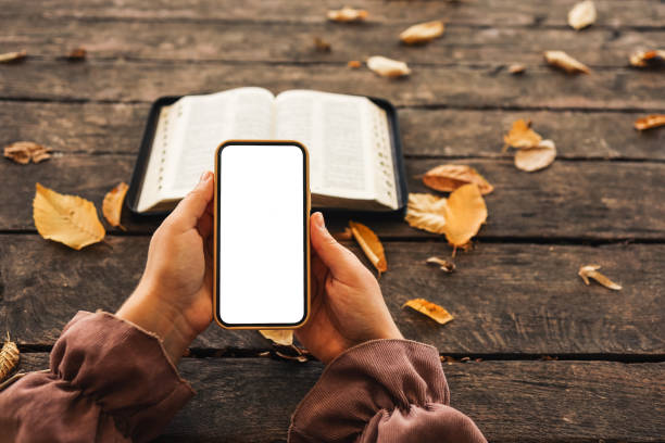 istock Open bible and phone with isolated screen on wooden background 1440368567