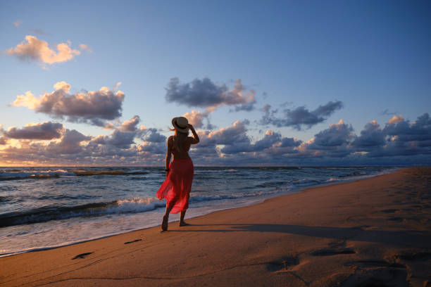 carefree woman in straw hat posing in the sunset on the sea beach. Vitality healthy living concept. Girl in pareo on sunset at stormy sea.