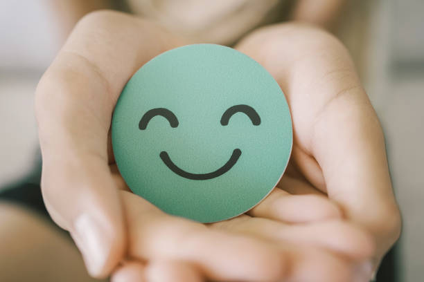 Hands holding green happy smile face paper cut, good feedback rating,think positive, customer review, assessment, child wellness,world mental health day, Compliment Day stock photo