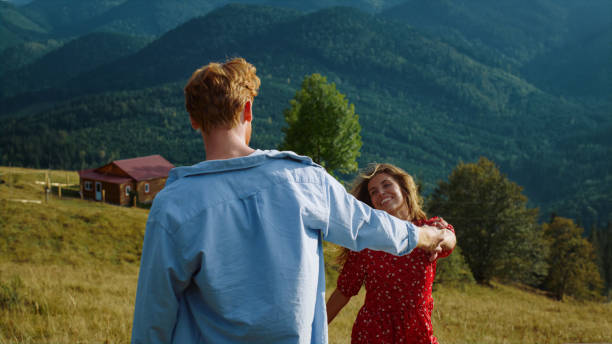 Lovely millennials hold hands on mountains walk. Young couple enjoy summer vacation together on green hill. Happy lovers have fun outdoors. Married family celebrate honeymoon. Nature travel concept.