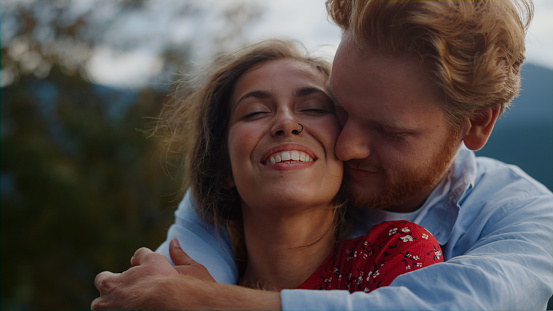 Portrait of happy man hugging woman outdoor. Young affectionate couple caressing each other in summer mountains. Tender lovers enjoying family vacation on meadow. Just married honeymoon concept