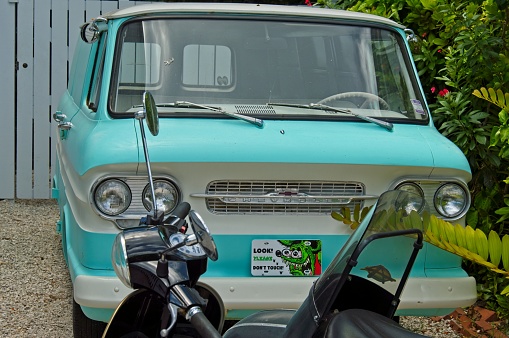 Early 1960s Chevrolet Corvair van painted in two toned white and aqua, May 2019. This preserved classic van in parked in a Key West Florida driveway with a motor scooter in front.