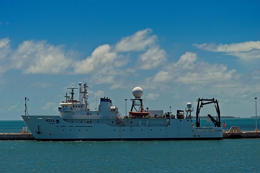 The NOAA research ship Okeanos Explorer docked at a Key West Florida pier, May 2019. Research vessel with blue skies and cumulus clouds in background.